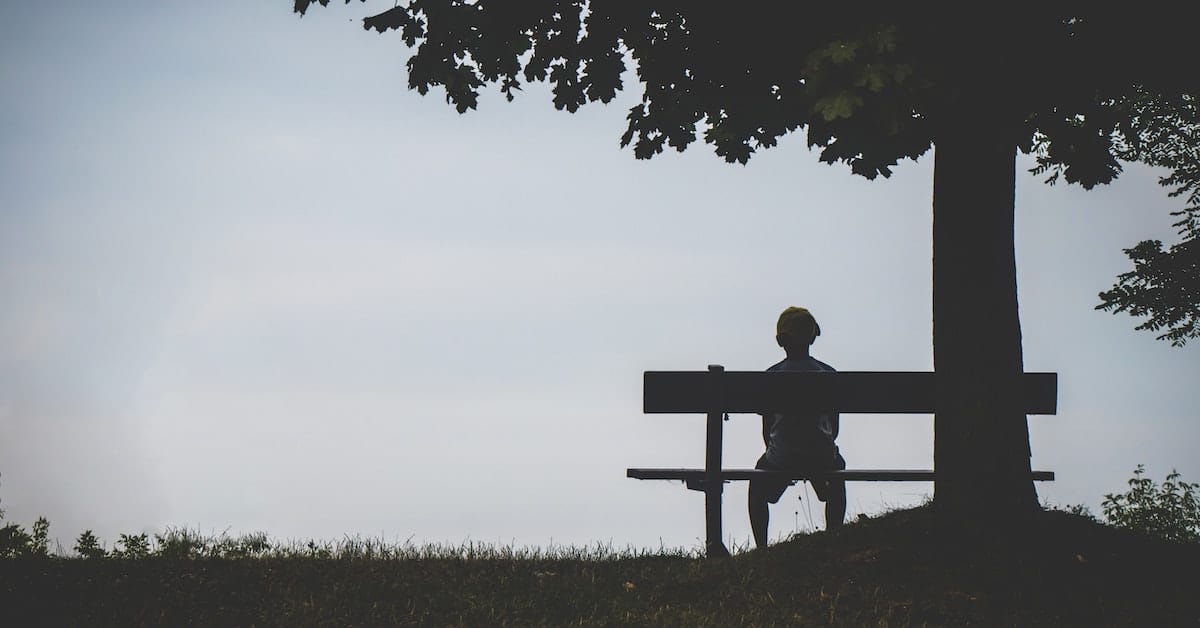 boy sitting on bench by tree not caring what others think
