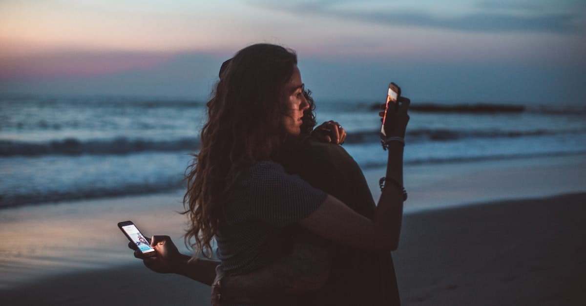 couple hugging on beach looking at smart phones caring too much what others think
